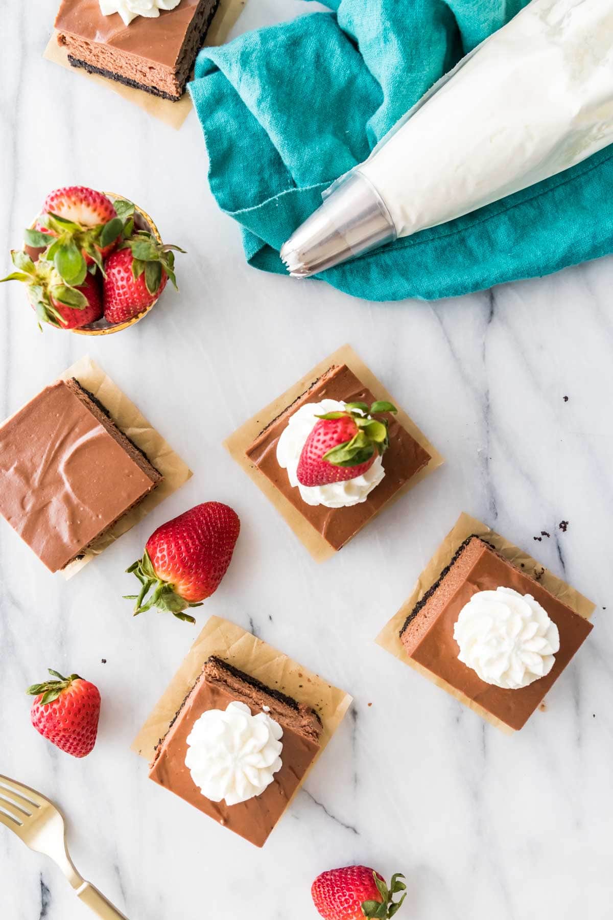 overhead view of chocolate flavored cheesecake bars topped with whipped cream and strawberries