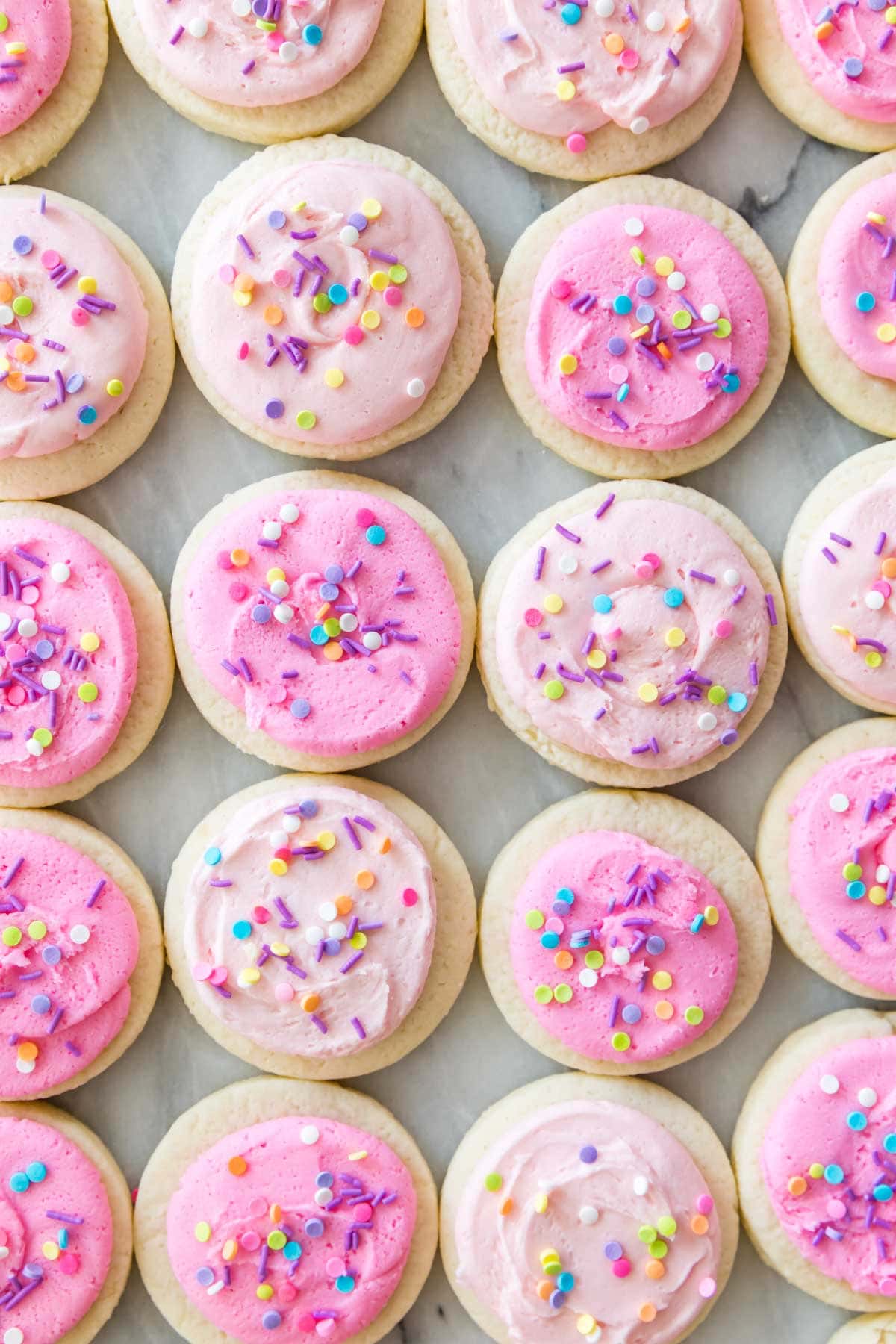 close-up overhead view of cookies topped with varying shades of pink icing and sprinkles
