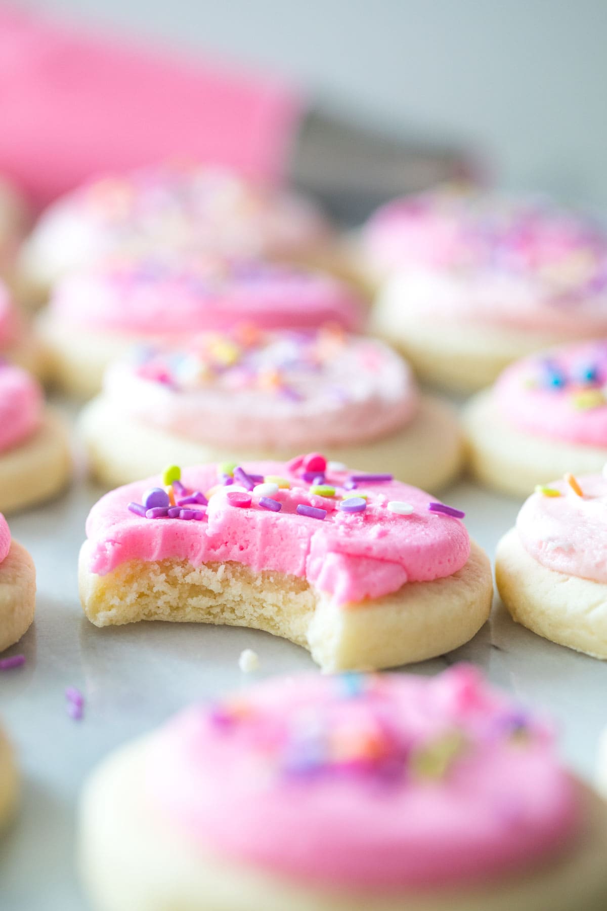 rows of perfectly round cookies topped with pink icing with the camera focused on one cookie that's missing a bite