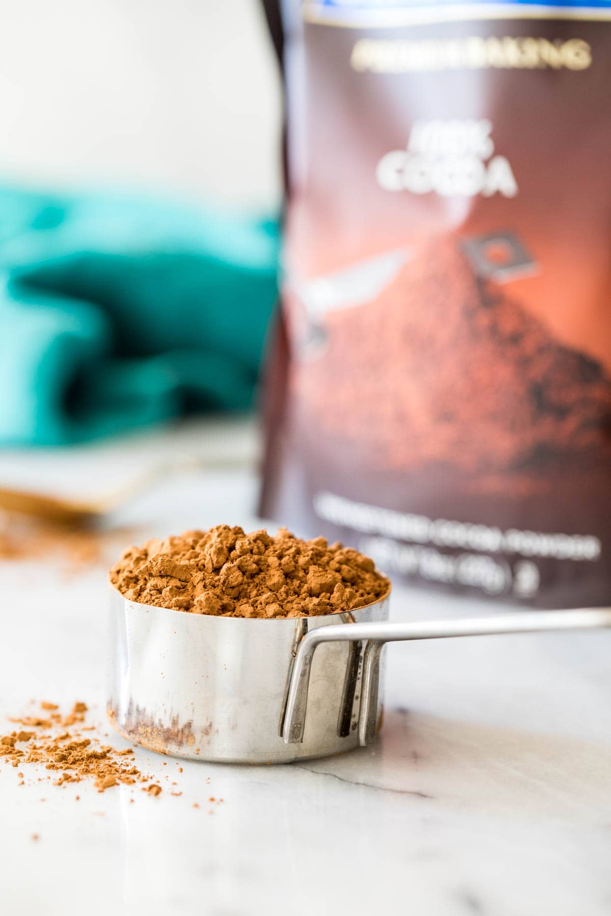 measuring cup of natural cocoa powder sitting in front of a bag of cocoa