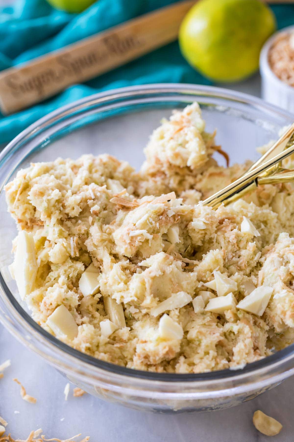 clear bowl of cookie dough with toasted coconut, lime zest, white chocolate chunks, and macadamia nuts mixed in