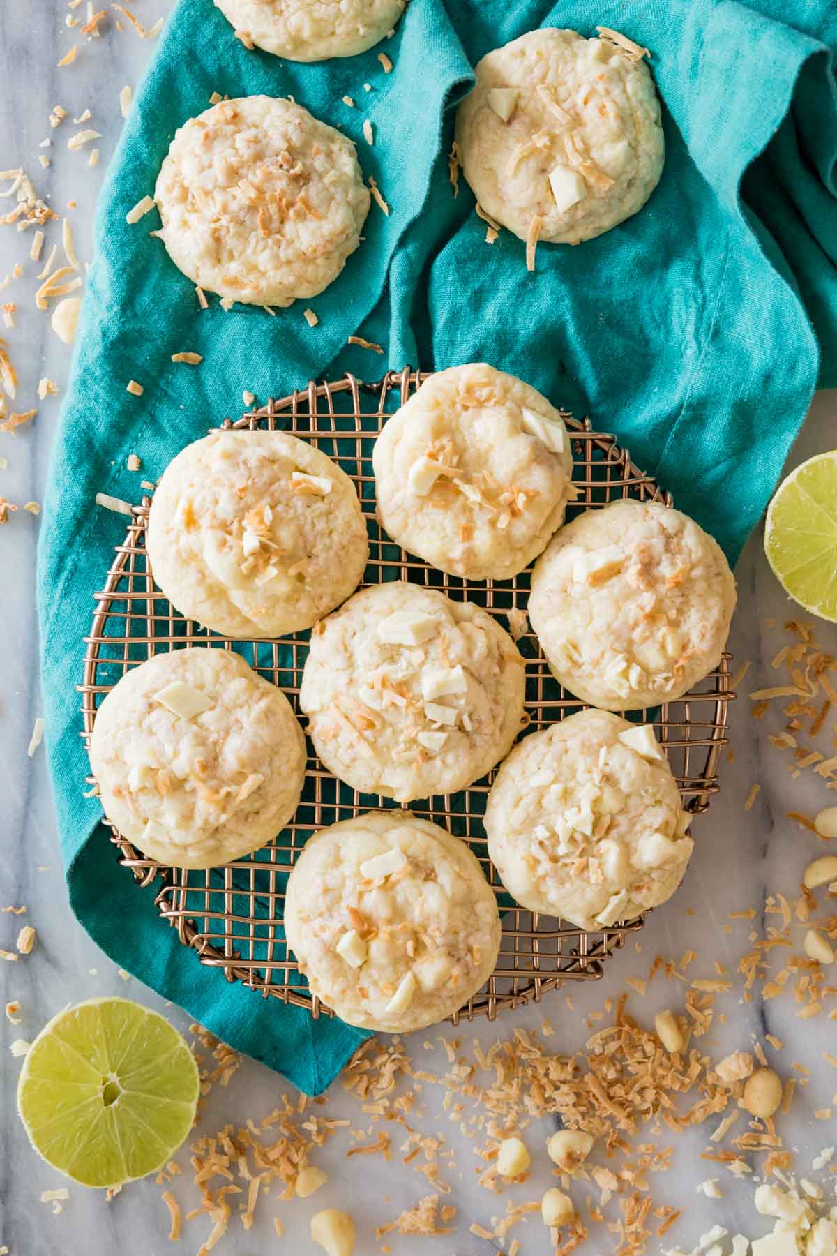 overhead view of cookies cooling on a metal rack surrounded by limes, toasted coconut, and macadamia nuts