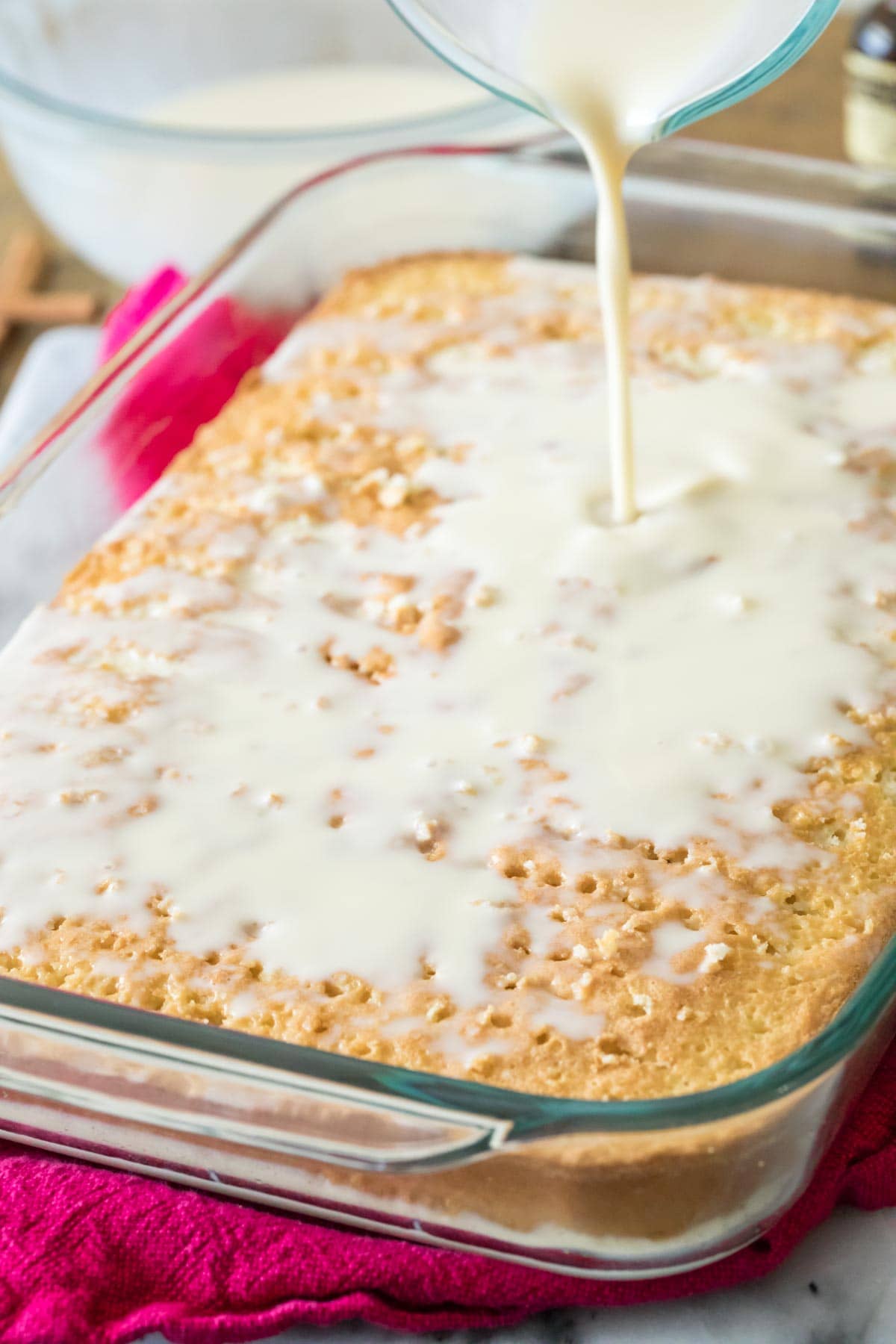 milk mixture being poured over a sheet cake with holes poked in it