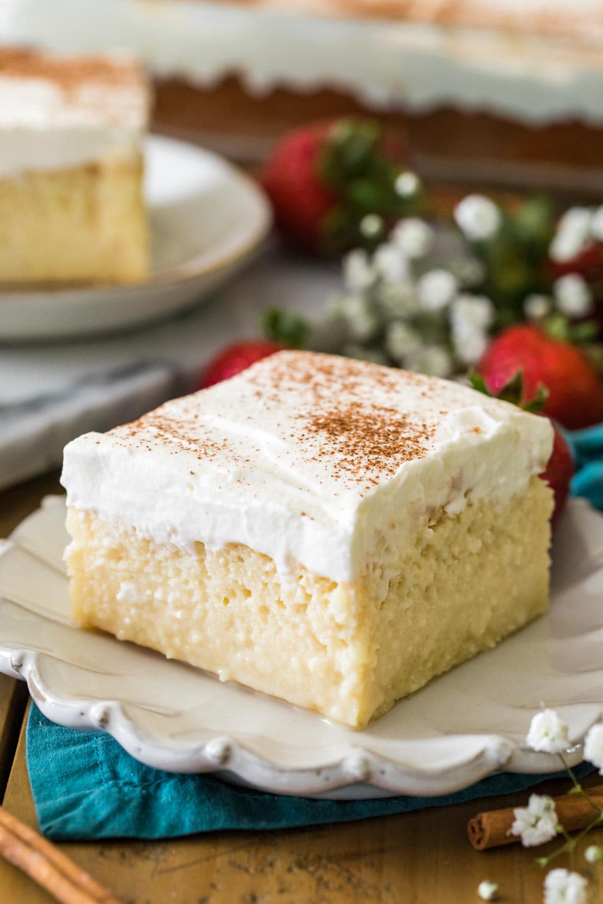 square slice of cake topped with whipped cream and cinnamon on a white decorative plate