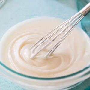 whisk stirring vanilla glaze in a clear glass bowl