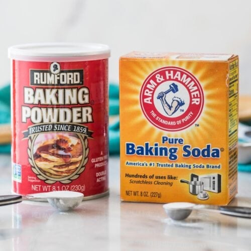photo comparing baking powder vs. baking soda side by side with measuring spoons of each in front of their respective containers