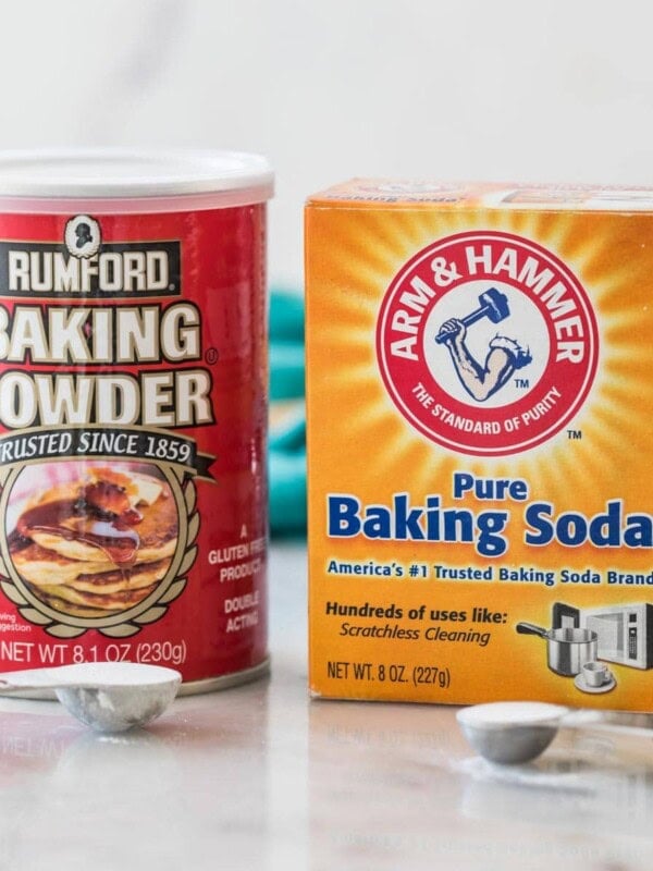photo comparing baking powder vs. baking soda side by side with measuring spoons of each in front of their respective containers