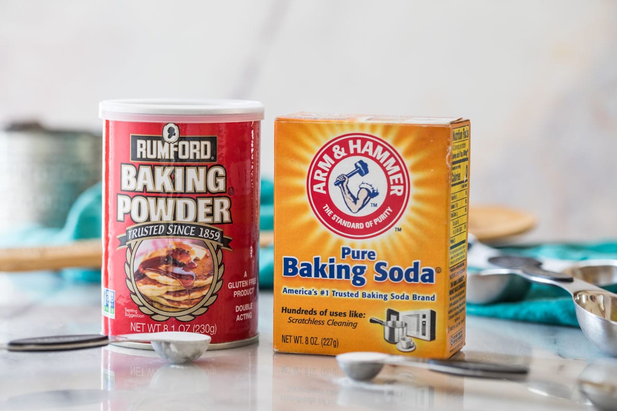 photo comparing baking powder vs. baking soda side by side with measuring spoons of each in front of their respective containers