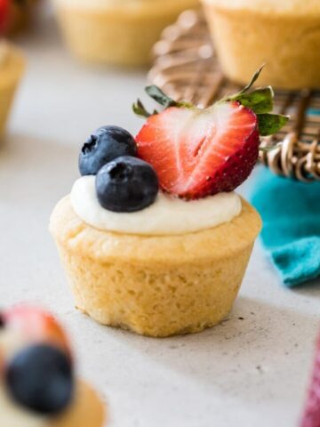 bite-sized cheesecake stuffed sugar cookie cup topped with two blueberries and a sliced strawberry half