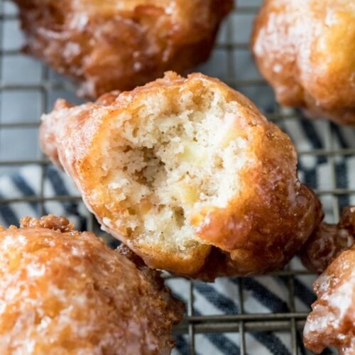 glazed apple fritters on a cooling rack with the center fritter missing one bite