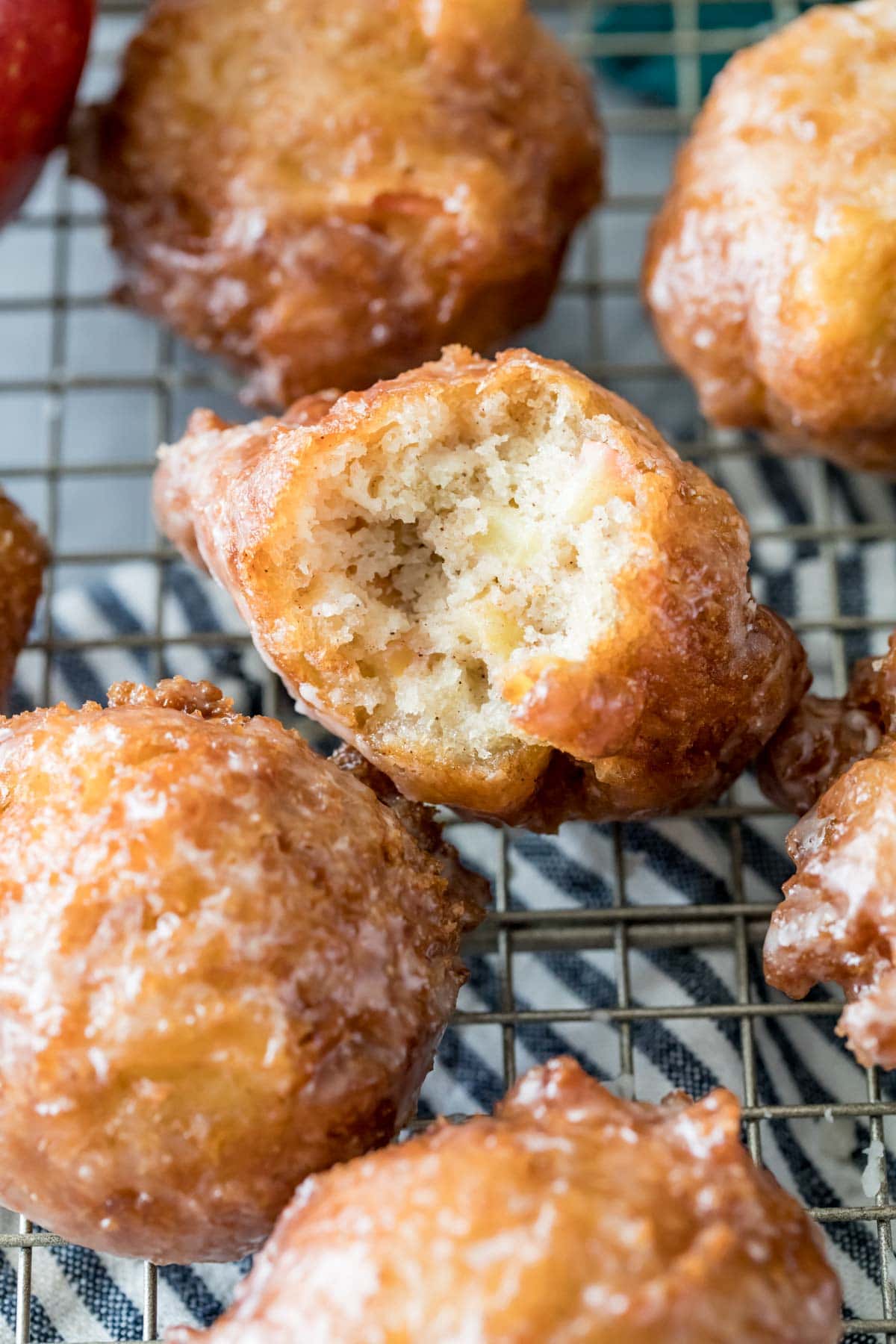glazed apple fritters on a cooling rack with the center fritter missing one bite