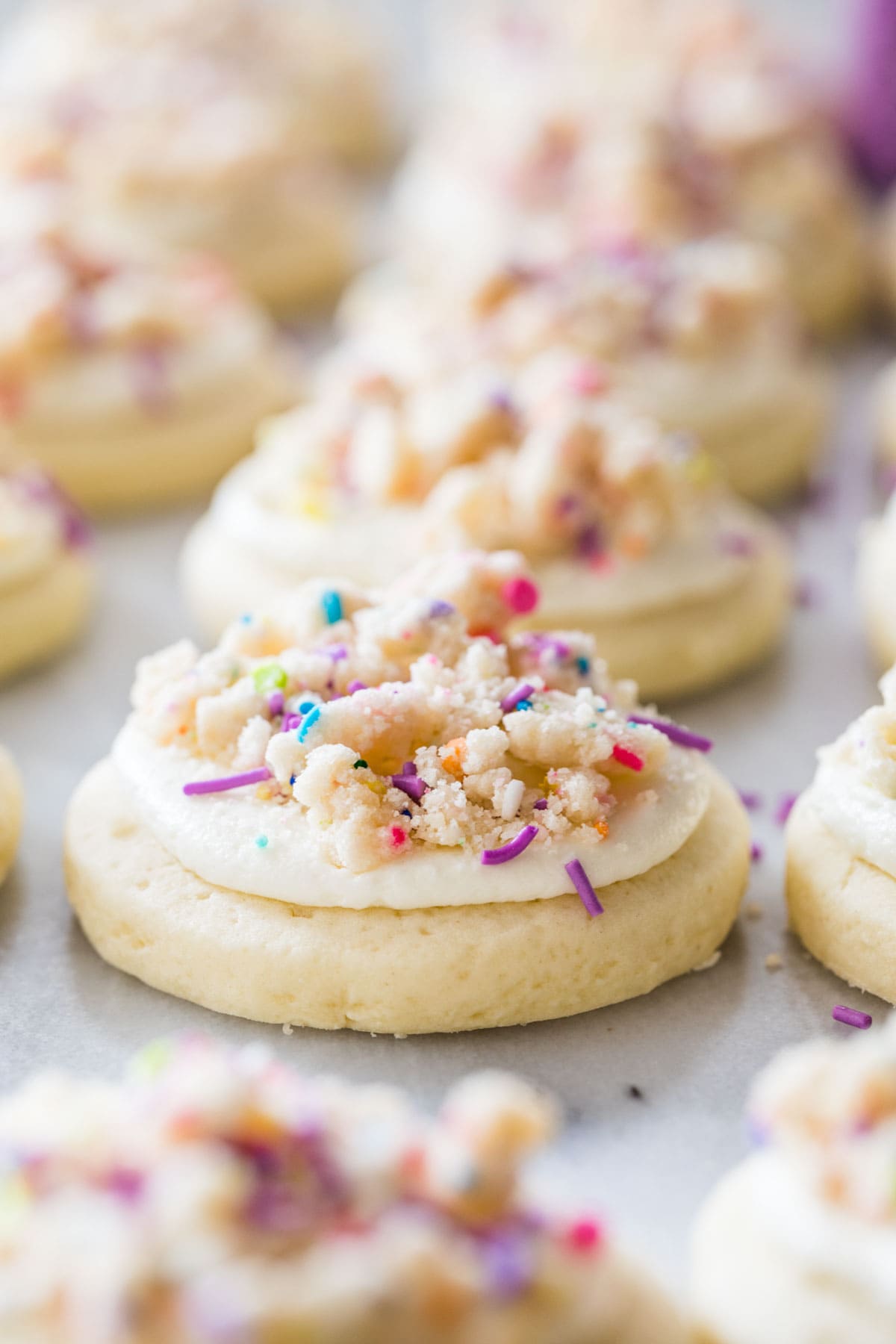 row of cookies topped with frosting, confetti cake crumbles, and sprinkles