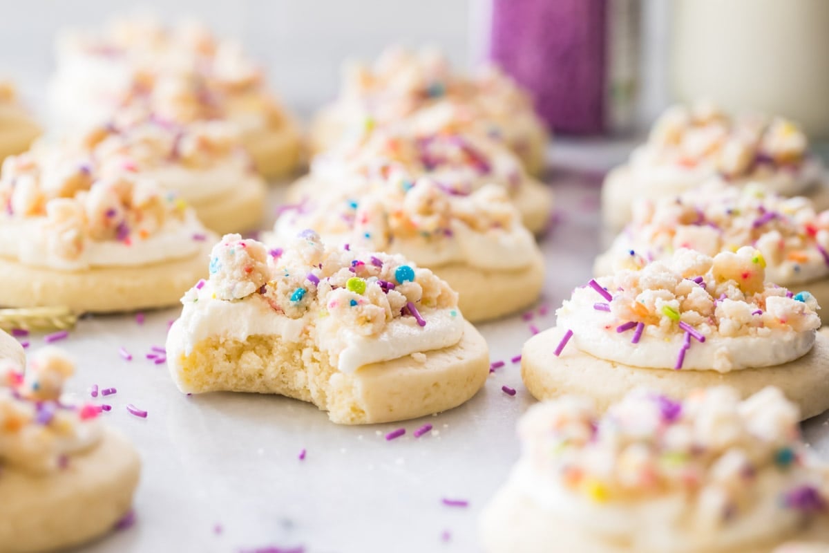 cookies topped with frosting and confetti cake crumbles with one cookie missing a bite