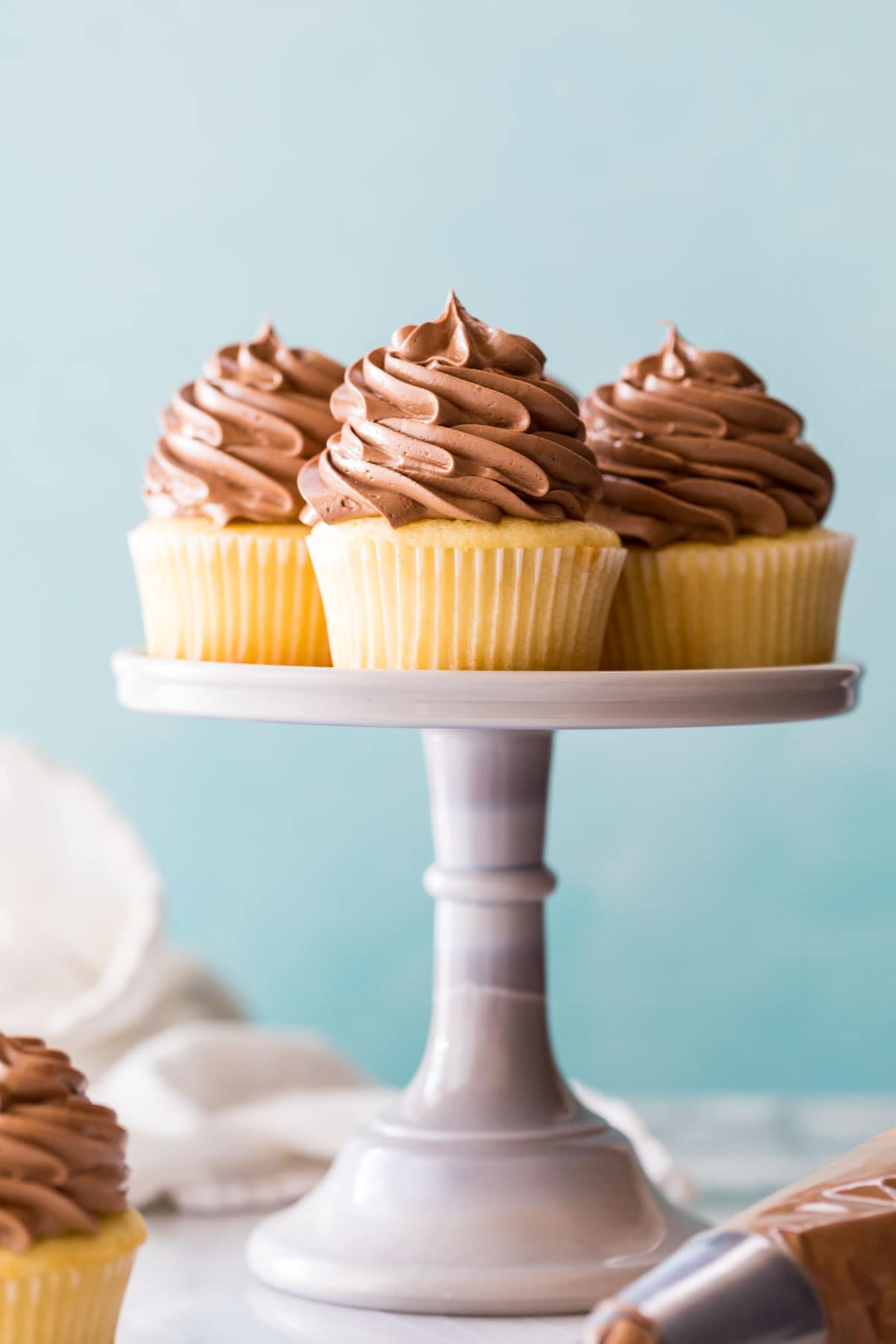 three yellow cupcakes topped with piped chocolate swiss meringue buttercream on a cake stand