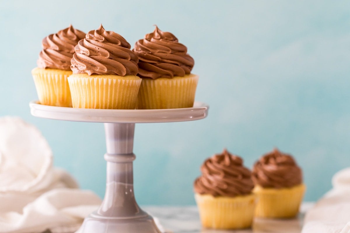 yellow cupcakes topped with chocolate frosting on a cake stand and countertop