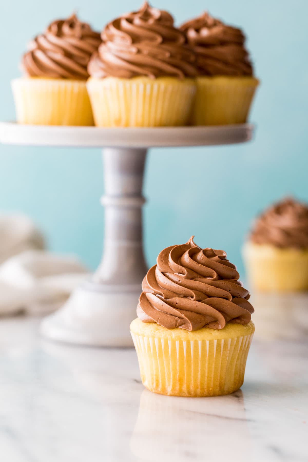 chocolate frosted yellow cupcake beneath a cake stand of more cupcakes
