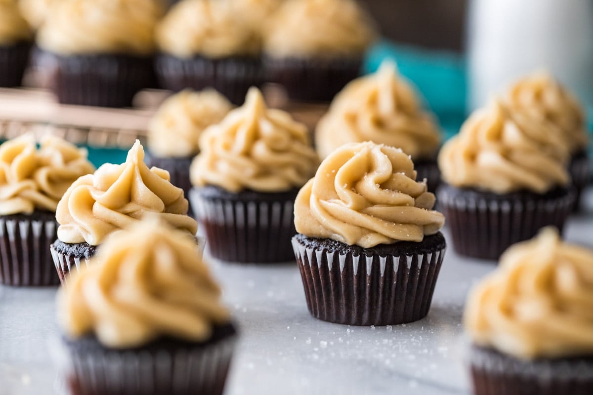 Dark chocolate mini cupcakes scattered across a white marble surface.