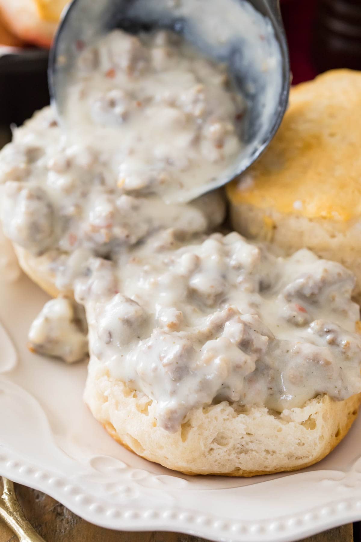 a ladle full of homemade sausage gravy recipe being poured over biscuits on white plate