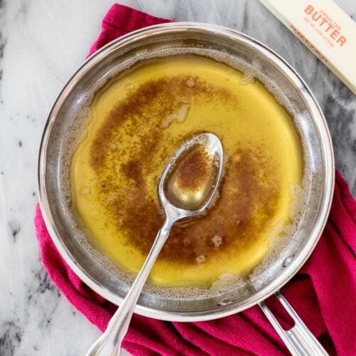 overhead view of a spoon resting in a stainless steel pan of brown butter