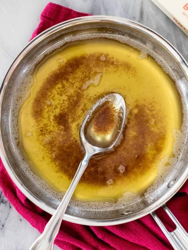 overhead view of a spoon resting in a stainless steel pan of brown butter