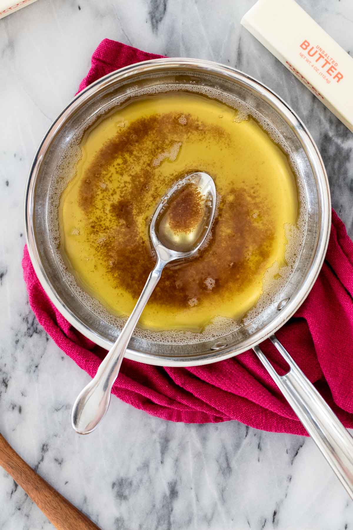 overhead view of a spoon resting in a stainless steel pan of brown butter