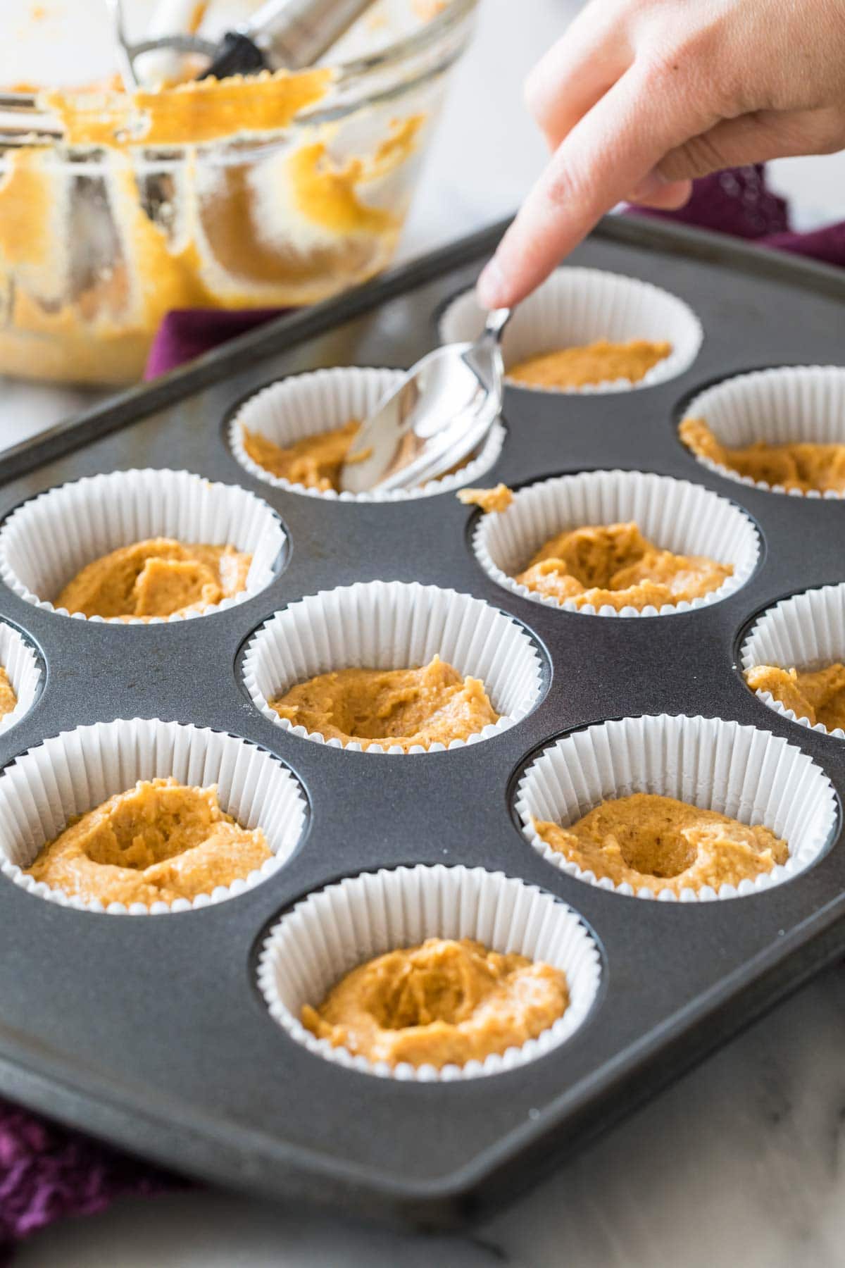 spoon creating small divots in unbaked pumpkin muffins