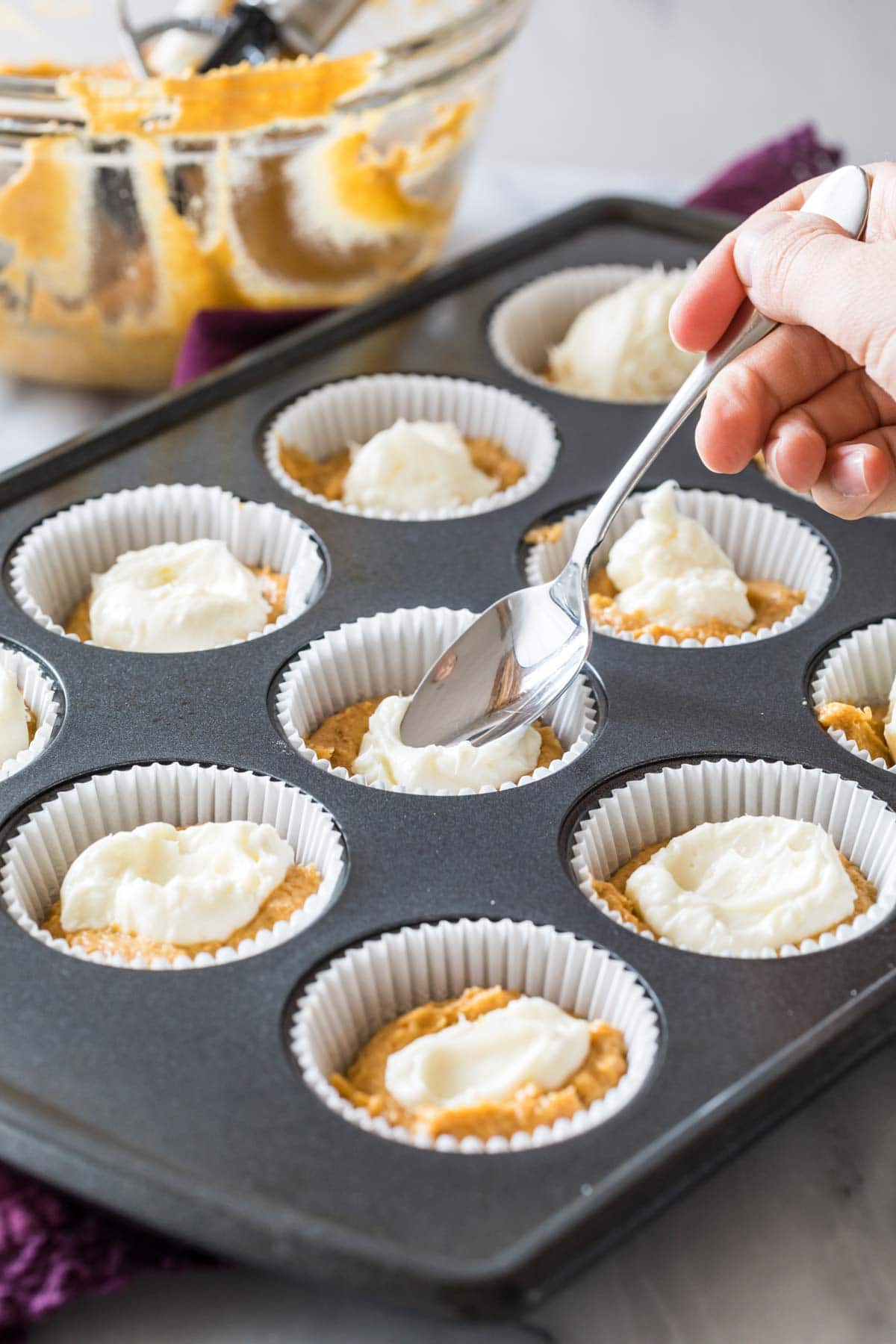 spoon adding a cheesecake filling to unbaked pumpkin muffins