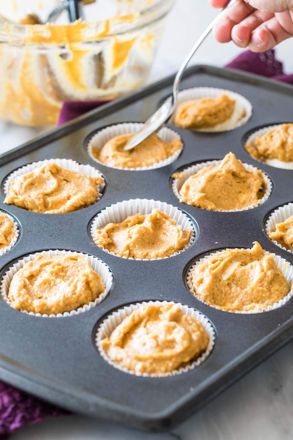 spoon smoothing pumpkin muffin batter into cupcake liners