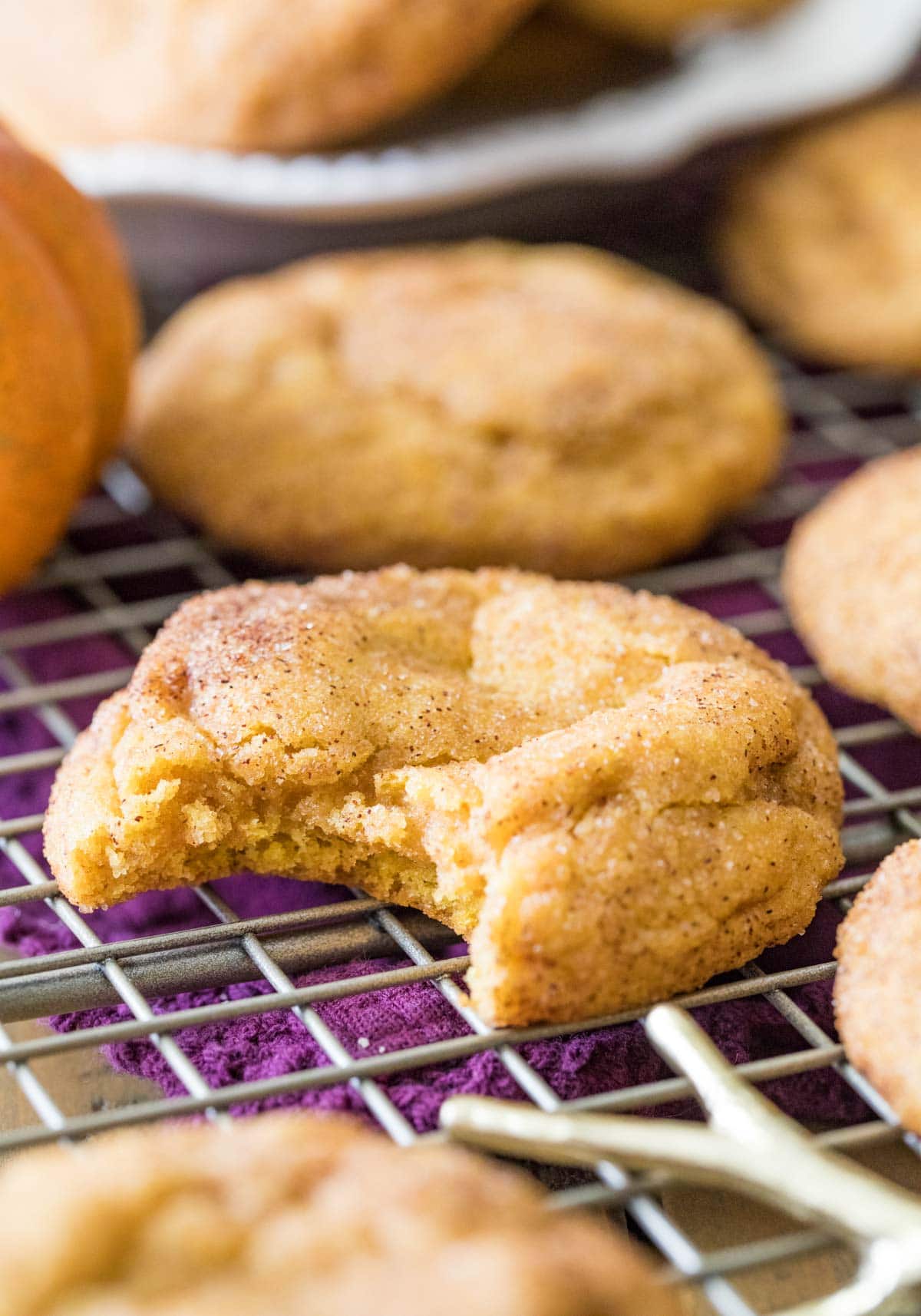 Pumpkin cookie missing a bite on a cooling rack surrounded by other cookies.