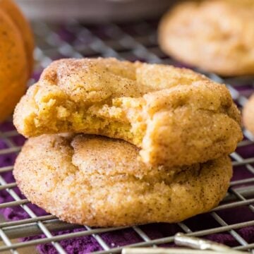 Two pumpkin snickerdoodles stacked on top of each other with the top cookie missing a bite.