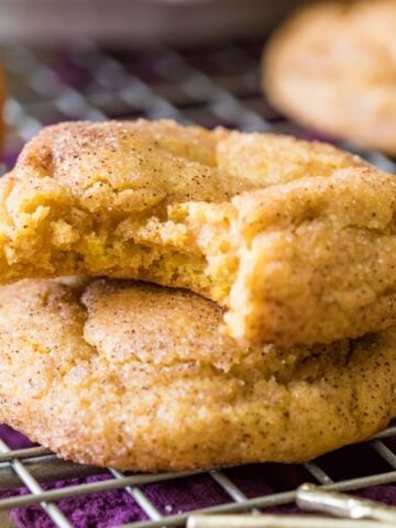 Two pumpkin snickerdoodles stacked on top of each other with the top cookie missing a bite.