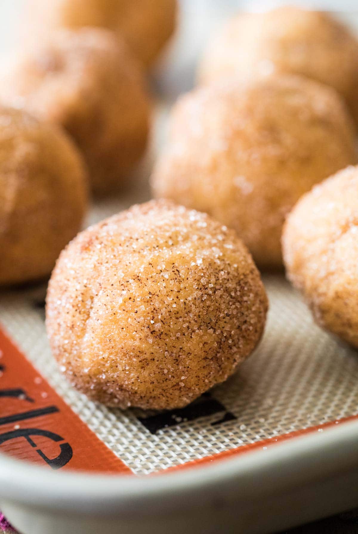 Balls of cinnamon sugar coated dough on a silicone baking sheet.