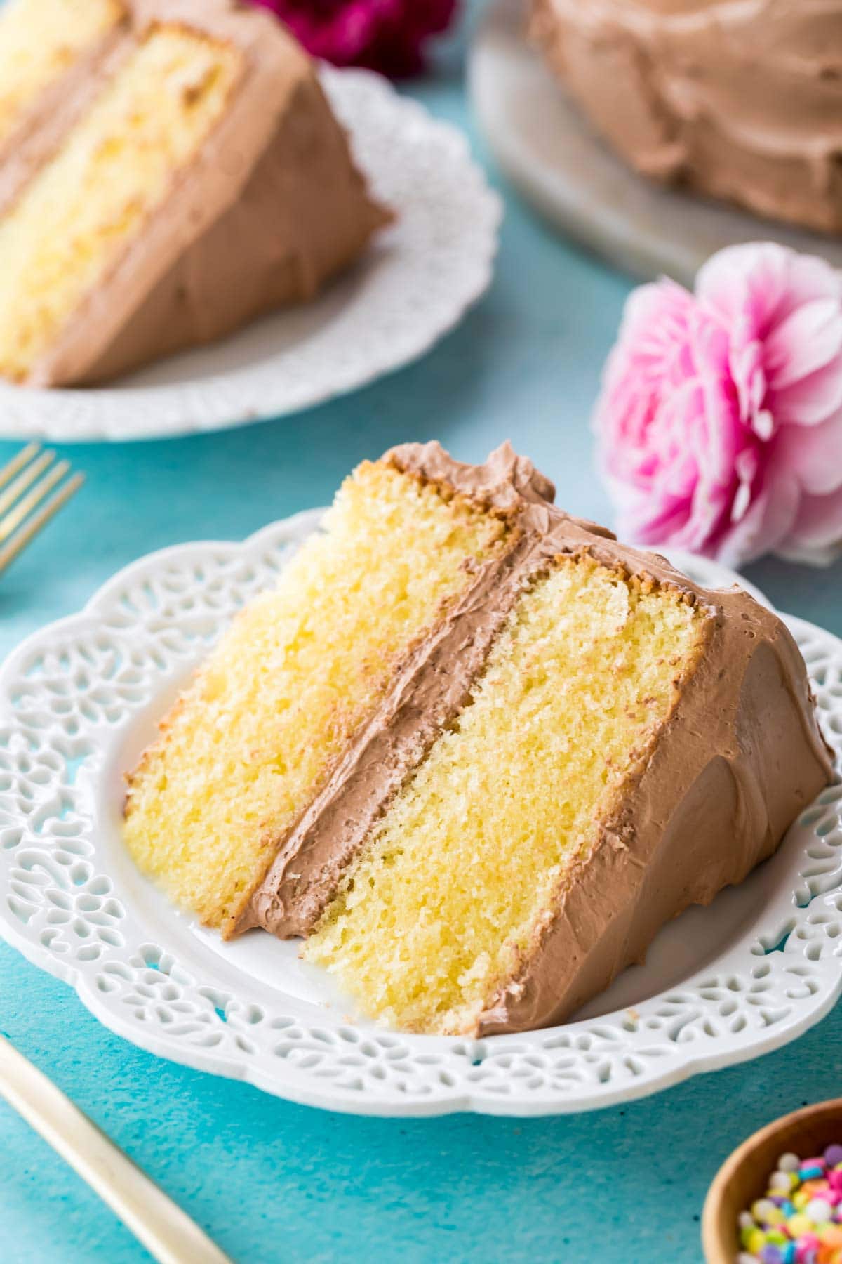 Overhead view of a slice of cake frosted with chocolate frosting on a white decorative plate.