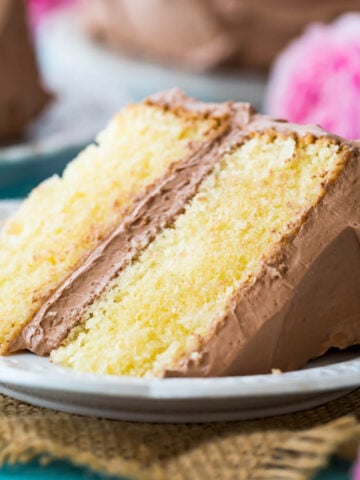 Two-layer slice of yellow cake frosted with chocolate frosting on a plate.