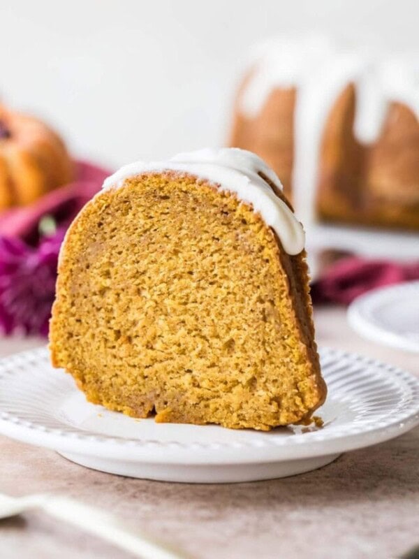 Slice of bundt cake topped with a thick white glaze standing up on a white plate.