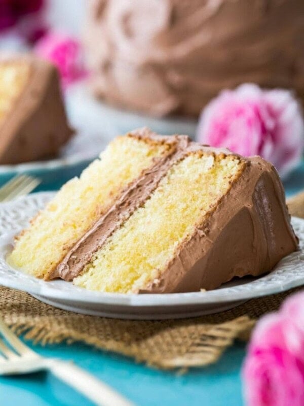 Two-layer slice of yellow cake frosted with chocolate frosting on a plate.