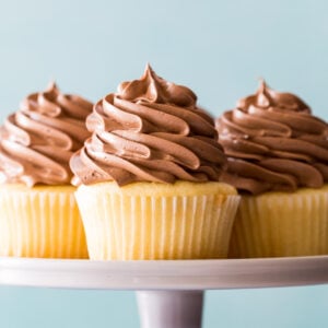 three yellow cupcakes topped with piped chocolate swiss meringue buttercream on a cake stand