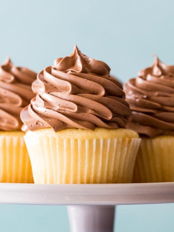 three yellow cupcakes topped with piped chocolate swiss meringue buttercream on a cake stand