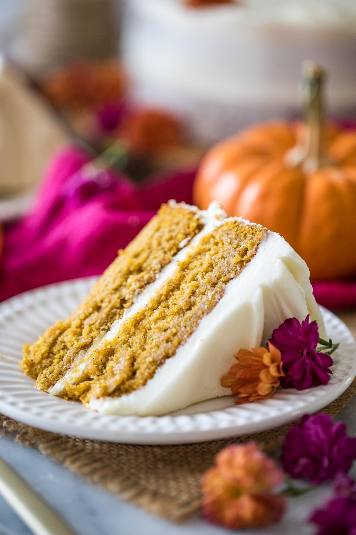 Slice of cake infused with pumpkin and spices frosted with cream cheese frosting on a white plate.