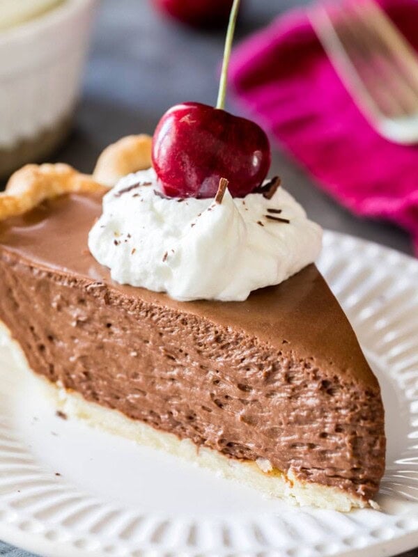Slice of French silk pie topped with whipped cream and a sweet cherry served on a white plate.