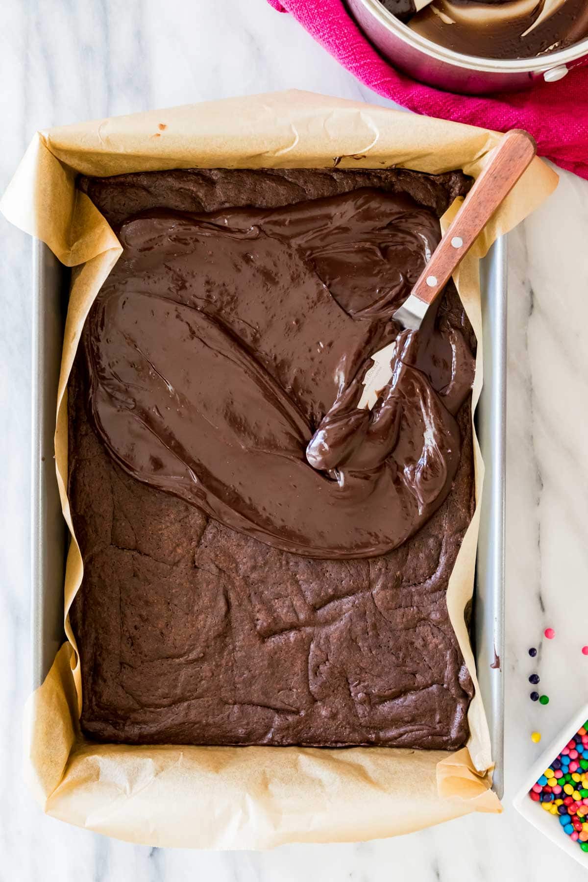 Fudgy chocolate frosting being spread onto a pan of brownies.