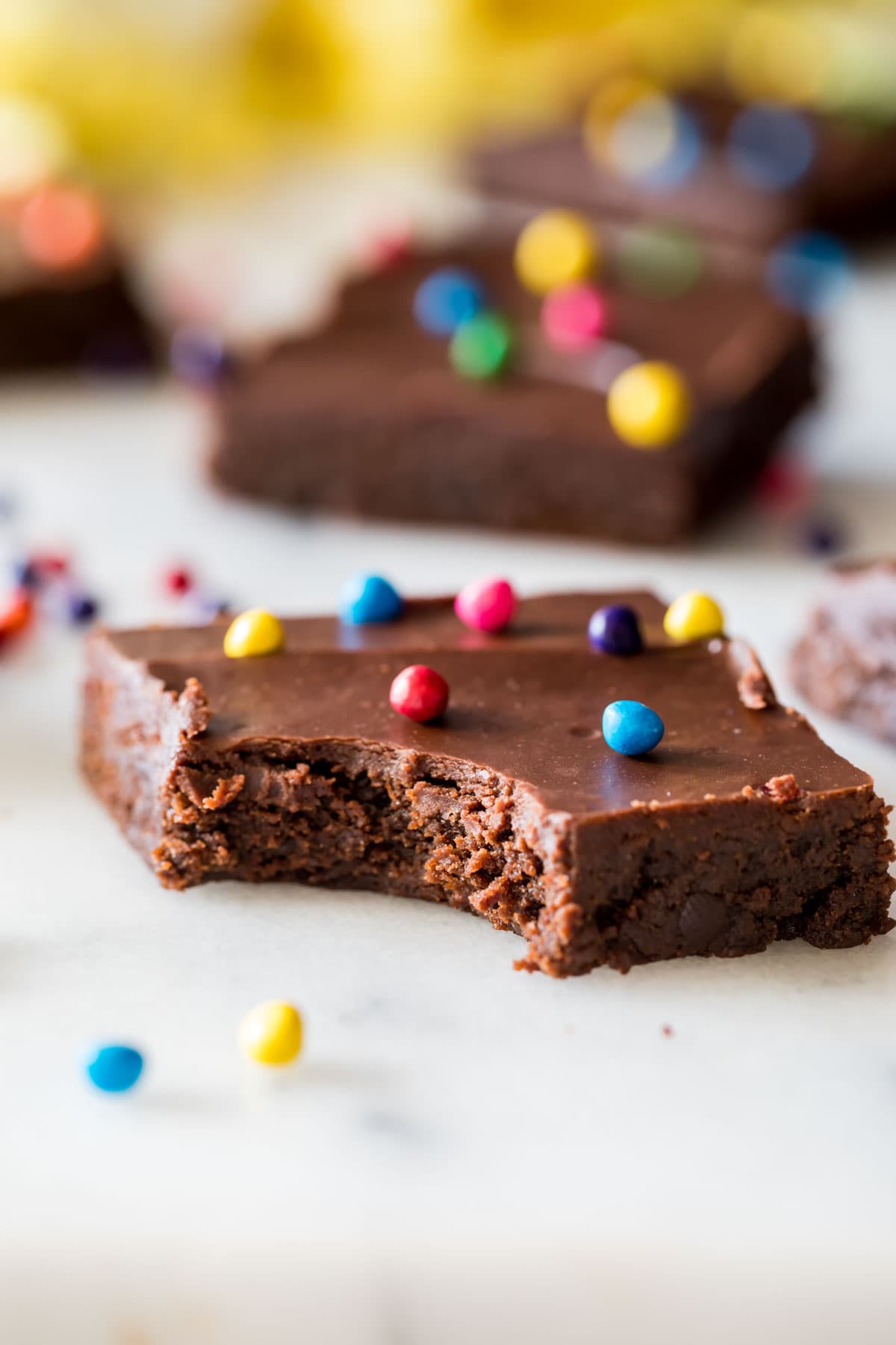 Fudgy chocolate brownie topped with colorful candies missing one bite.