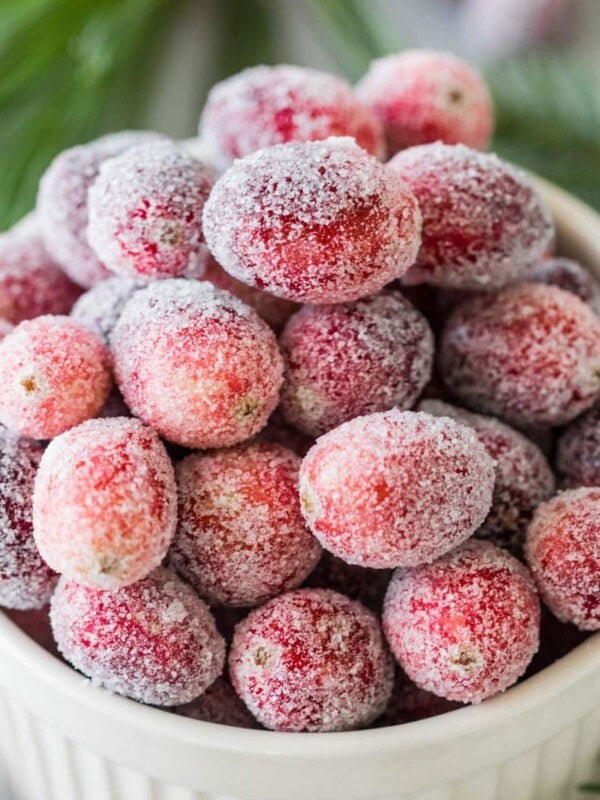 Overhead view of sugared cranberries in a white bowl.