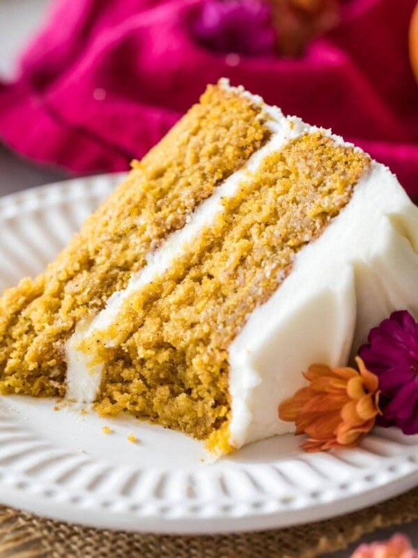Slice of pumpkin cake frosted with cream cheese frosting on a white plate.