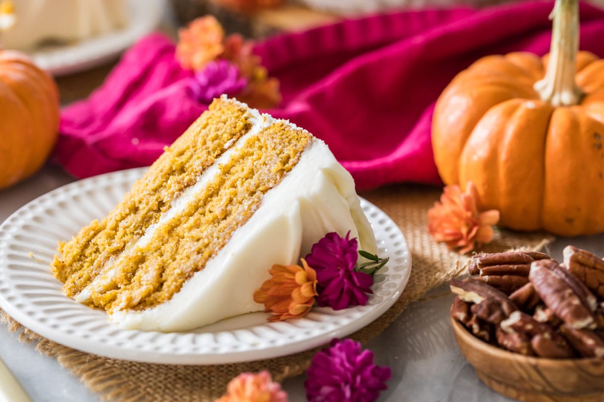 Slice of cake infused with pumpkin and spices frosted with cream cheese frosting on a white plate.