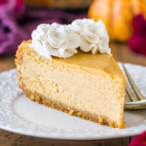 Slice of pumpkin cheesecake topped with cinnamon whipped cream on a white plate.