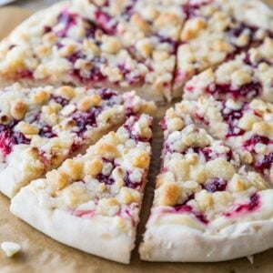 Close-up view of a raspberry cheesecake dessert pizza topped with white chocolate chips and streusel.