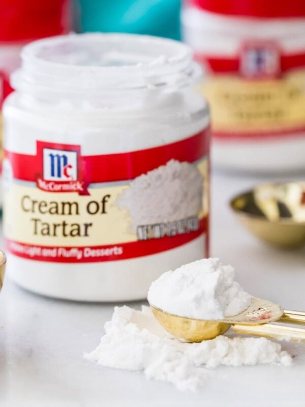 Small open jar of cream of tartar with a gold measuring spoon of cream of tartar beside it.