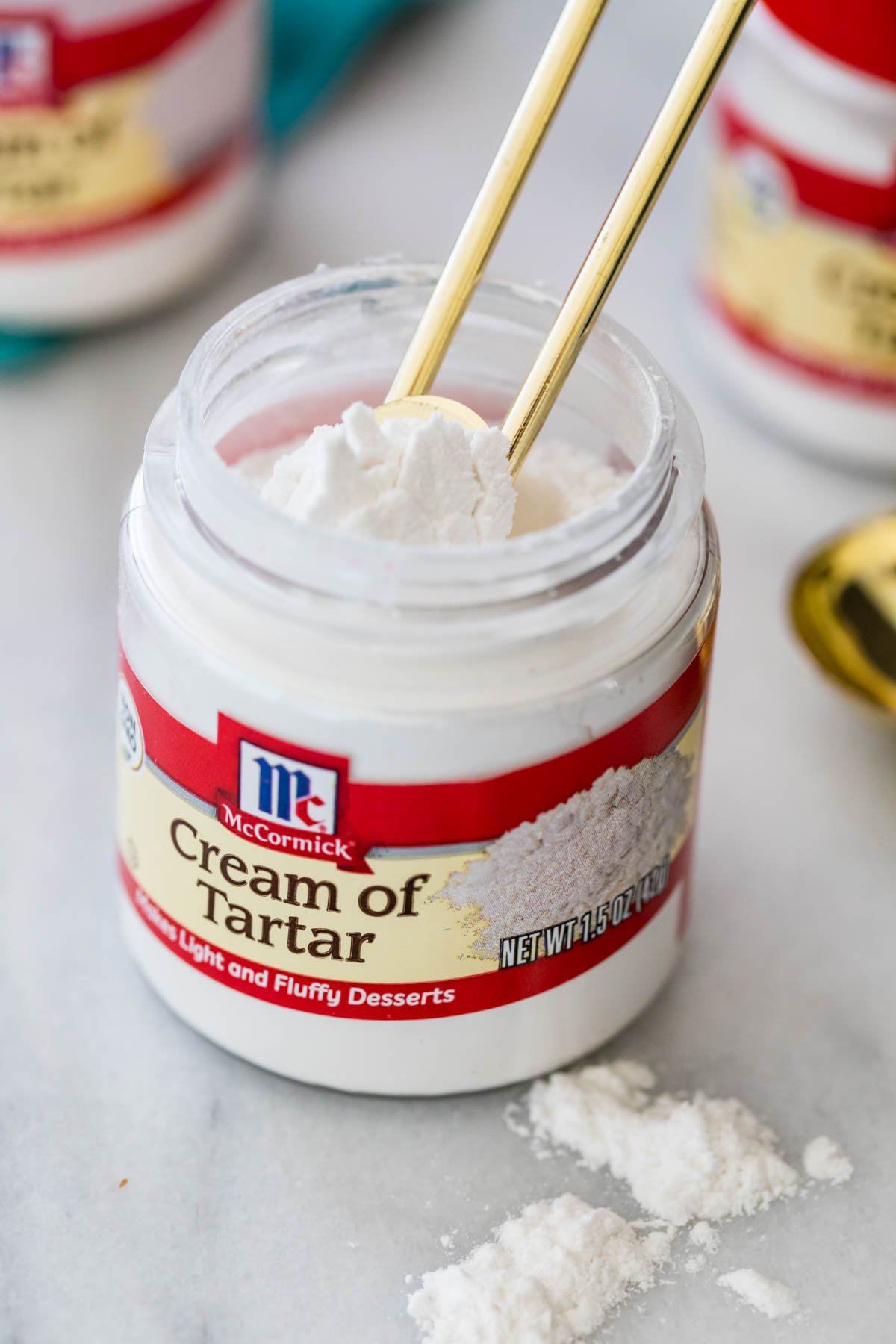 Overhead view of a gold measuring spoon scooping cream of tartar out of its container.