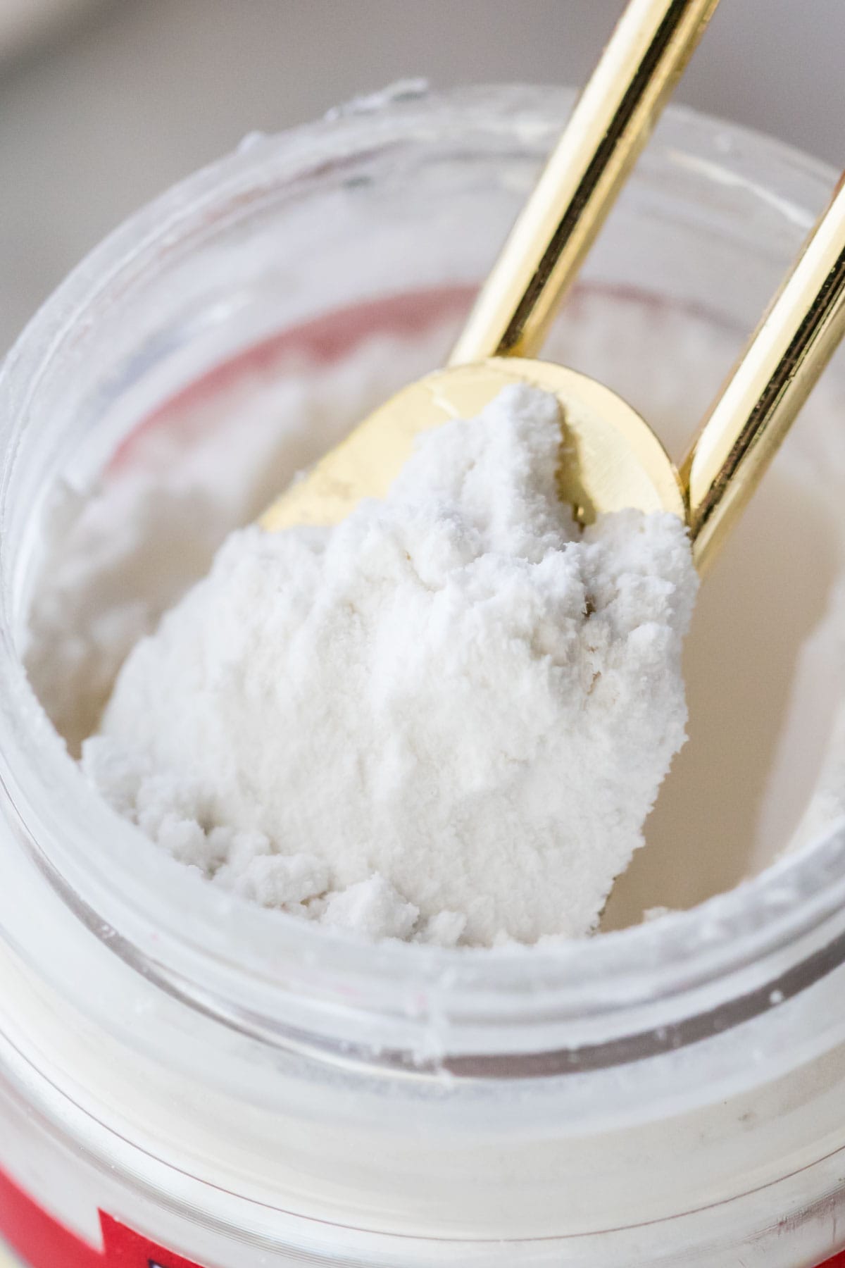 Close-up of a gold measuring spoon scooping white powder out of a small container.